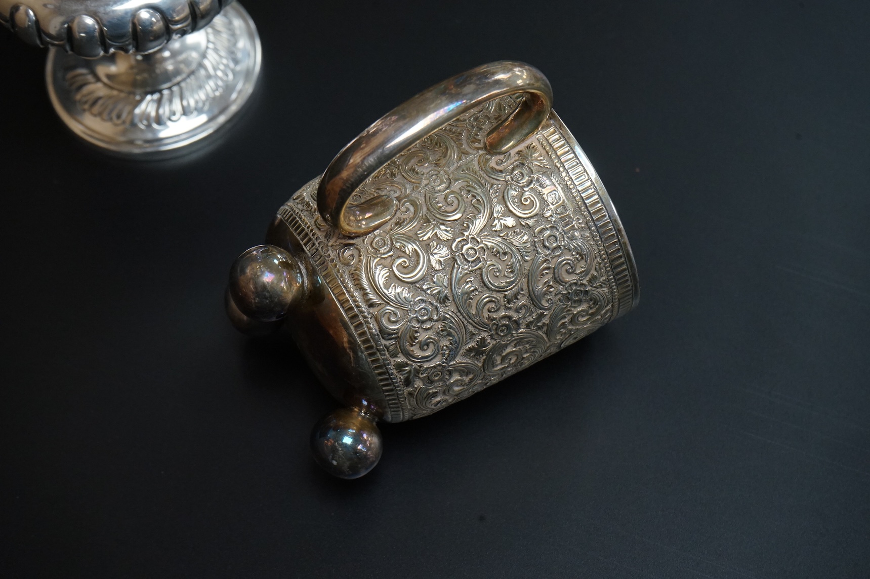 A Victorian embossed silver christening mug, on three ball feet, Martin, Hall & Co, London, 1874, height 85mm, together with a similar sugar caster, Lee & Wigful, Sheffield, 1899.